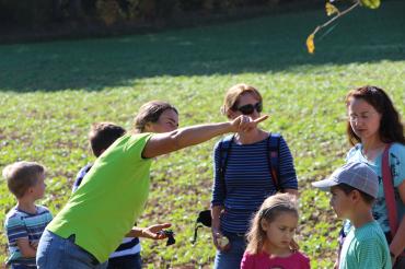 Zu sehen ist eine Frau, welche vor einer Gruppe Menschen mit dem Finger auf etwas in der Natur zeigt.