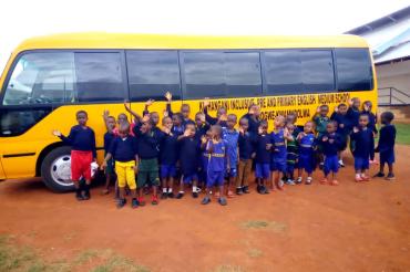 Das Bild zeigt Kinder vor ihrem neuen Schulbus in Tansania.