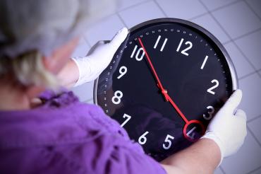 Zu sehen ist eine Person, welche eine Uhr in den Händen hält.