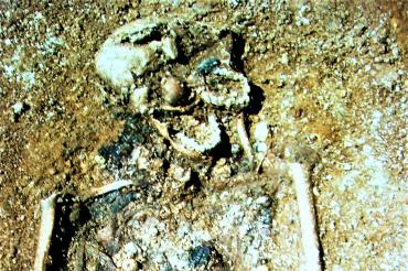 Zu sehen ist ein offenes Grab mit einem Skelett. 