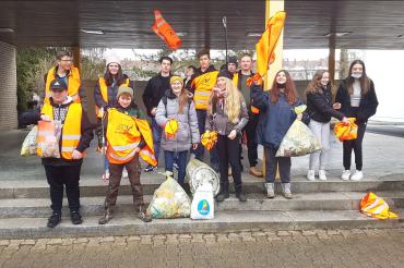 Zu sehen ist die Klasse 8 b nach der Müllsammelaktion in Warnwesten mit dem gesammelten Müll. 