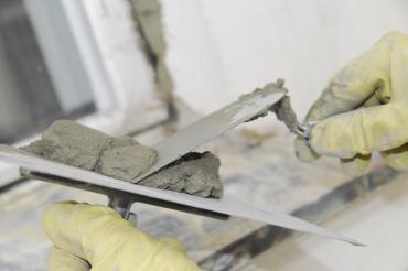 Zu sehen ist eine Maurerkelle, die von zwei Händen gehalten wird. 