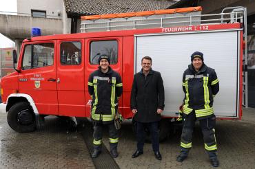 Zu sehen sind zwei Feuerwehrmänner und der Donauwörther Oberbürgermeister, welche vor einem Feuerwehr stehen.