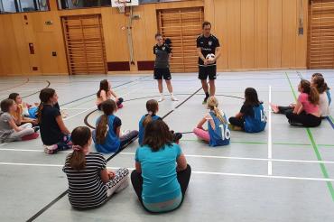 Zu sehen sind Markus und Sarah, wie sie den Schülerinnen etwas erklären. 