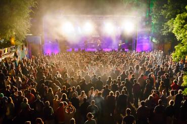 Zu sehen ist eine Bühne in hellem Licht mit vielen Zuschauern davor. 