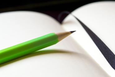 Zu sehen ist ein Bleistift der auf einem offenen Buch liegt. 
