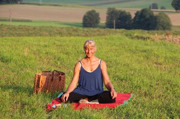 Zu sehen ist eine Frau auf einer Wiese im Schneidersitz. 