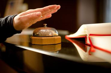 Hand auf Klingel an Hotelrezeption. 
