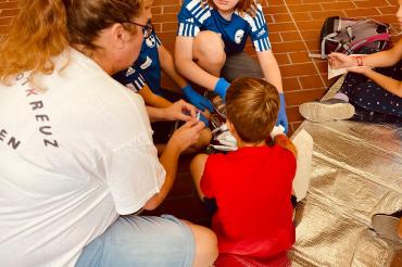 Das Bild zeigt eine Gruppe von Kindern, die sich beim Ferienprogramm die geschminkten Wunden gegenseitig verarzten.