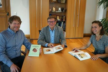 Die beiden Kreisfachberater für Gartenkultur und Landespflege Paul Buß und Sophia Och stellen Landrat Stefan Rößle (Bildmitte) das neue und doch auch alte Buch "Abbildung von Rieser Obstsorten" vor.