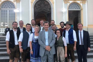 Das Foto zeigt Ministerpräsident Markus Söder und MdL Wolfgang Fackler mit der Musikkapelle „United Blech“ vor dem Neuen Schloss Schleißheim.