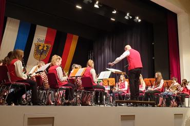  „In den Farben getrennt, in der Sache vereint!“ Das gilt auch für das äußere Erscheinungsbild des Doppel-Vororchesters. Die roten Westen für die Stadtkapelle sind pünktlich zum Konzert fertig geworden. So trugen die Musiker*innen dieses Ensembles schwarze Hose, weiße Bluse bzw. Hemd und rote Weste -  die Buben der Knabenkapelle ihre gewohnte schmucke Uniform. Auch Körner hatte eine rote Weste an.