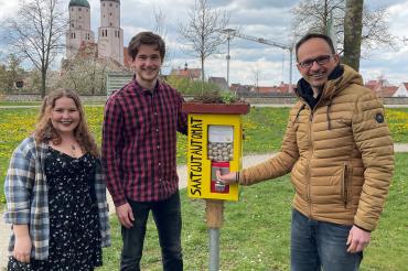Sophie Fischer und Simon Strohofer zeigen Bürgermeister Martin Drexler den neuen Saatgutautomat am Johannisweiher. 
