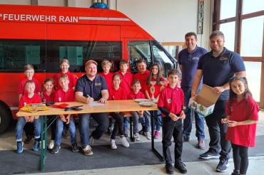 Die Kinder der Kinderfeuerwehr Rain am Lech beim Ziehen der Lose zusammen mit dem Organisationsteam Kreisjugendwart Markus Meyr (sitzend), Jugendwart der Freiwilligen Feuerwehr Rain am Lech Philipp Marb und Inspektionsjugendwart Stefan Eder.