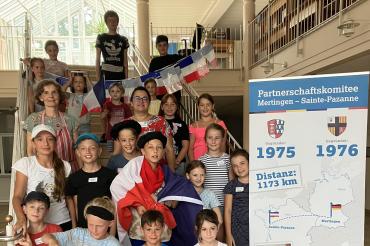 Marita Braun und Christine Riepold, Vorsitzende des Partnerschaftskomitees, mit den Kindern des Ferienprogramms in der Aula der Grundschule Mertingen.