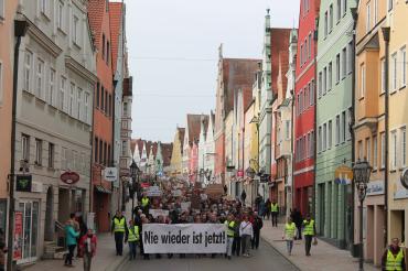 Das Bild zeigt die Demonstrant*innen in der Donauwörther Reichsstraße. Auf einem Banner steht: Nie wieder ist jetzt.