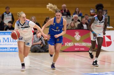 Drei Basketballerinnen, zwei kämpfen um einen Ball, eine hat ein Blaues Trikot an, die andere hat ein Weißes Trikot an