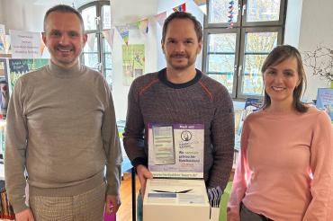 Drei Menschen, die Person in der Mitte hält eine Box.