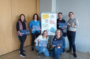 4 Personen Hinten die Stehen, Zwei Personen vorne die Knieen. Alle Schauen in die Kamera und Lächeln.