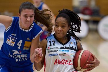 Zwei Frauen der Basketball Spielen, die linke hat ein blaues Trikot an und die rechte ein Weißes. Die rechte Frau hat auch einen Basketball unter ihren Arm.
