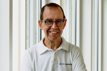 Mann mit weißem Poloshirt  der die Arme verschränkt 