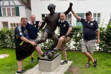 Hier sieht man vier schottische Fußballfans an der Gerd-Müller-Statue in Nördlingen.