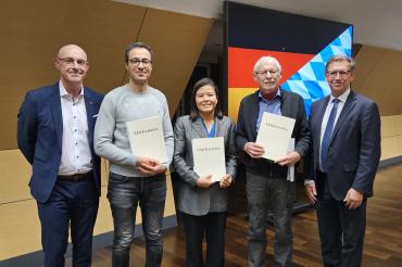 Drei neue Staatsbürger präsentieren ihre Urkunden, begleitet von Johann Stark, Fachbereichsleiter Personenstands- und Ausländerwesen, Staatsangehörigkeitsrecht und Landrat Stefan Rößle, die die Verleihung würdigten.