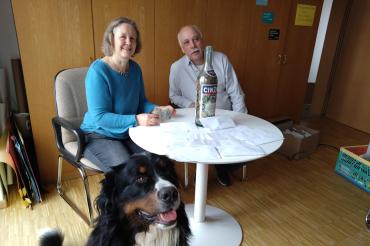 zwei Menschen sitzen an einem Runden Tisch, davor ein Hund