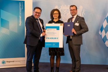 Staatssekretär Tobias Gotthardt, Regionalmanagerin Laura Brummer und Stabstellenleiter Klemens Heininger bei der feierlichen Übergabe des Förderbescheids.