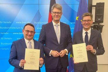 Ulrich Lange (l.) erhält die Urkunde vom neuen Verkehrsminister Patrick Schnieder (M.).