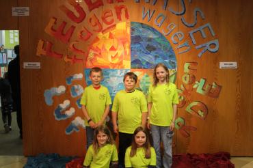 Amerdinger Grundschule in den neuen Schul-Shirts vor dem Wandgemälde im Eingangsbereich.