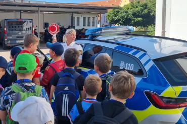 Teilnehmende Kinder und Polizistin Frau Stephanie Mergel vor einem Dienstwagen.