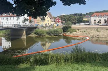 Die Feuerwehr will durch Barrikaden ein Eindringen des Ölteppichs in die Wörnitz verhindern.