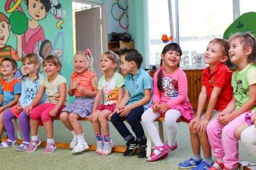 Mehrere Kinder sitzen in einer Reihe in einem Kindergarten.