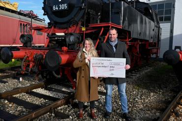 Barbara Wunder und Patrick Zeitlmann bei der Scheckübergabe vor historischer Kulisse im Bayerischen Eisenbahnmuseum Nördlingen.