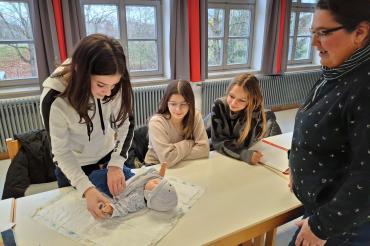 Das Bild zeigt, wie die Teilnehmenden das Wickeln eines Kleinkindes unter Anleitung der Facherzieherin Stefanie Baumgärtel trainieren. 