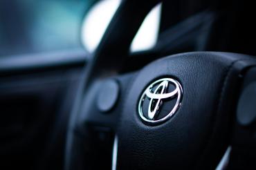Schwarzes Lenkrad mit silbernem Toyota-Logo aus Metall.