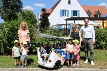 Simon Rupprecht von der Raiffeisen-Volksbank Ries übergibt den Kinderbus an die Krippenerzieherinnen Svenja und Veronika im Gemeinde-Kindergarten Otting.