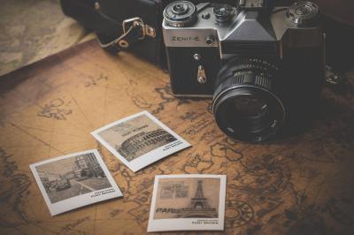 Auf dem Bild sieht man eine alte Kamera. Vor ihr liegen Polaroid Bilder von Reisen.