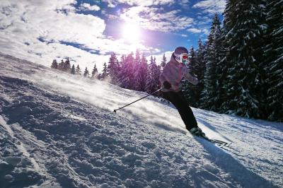 Skifahrerin fährt Berg hinunter, dahinter Bäume und tiefstehende Sonne
