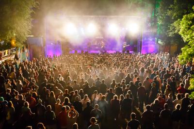 Zu sehen ist eine Bühne in hellem Licht mit vielen Zuschauern davor. 