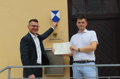 Nördlingens Oberbürgermeister David Wittner (l.) und Stadtarchivar Dr. Johannes Moosdiele-Hitzler präsentieren das Schutzschild und die Urkunde.