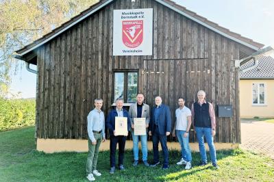 Sechs Männer stehen lächelnd im Freien vor dem Vereinsheim in Dornstadt. In der Mitte hält Ingo Steinbrecher vom Amt für Ländliche Entwicklung die offizielle Einleitungsurkunde der Dorferneuerung in den Händen, flankiert von den Vertretern der Gemeinde und der Arbeitskreise.