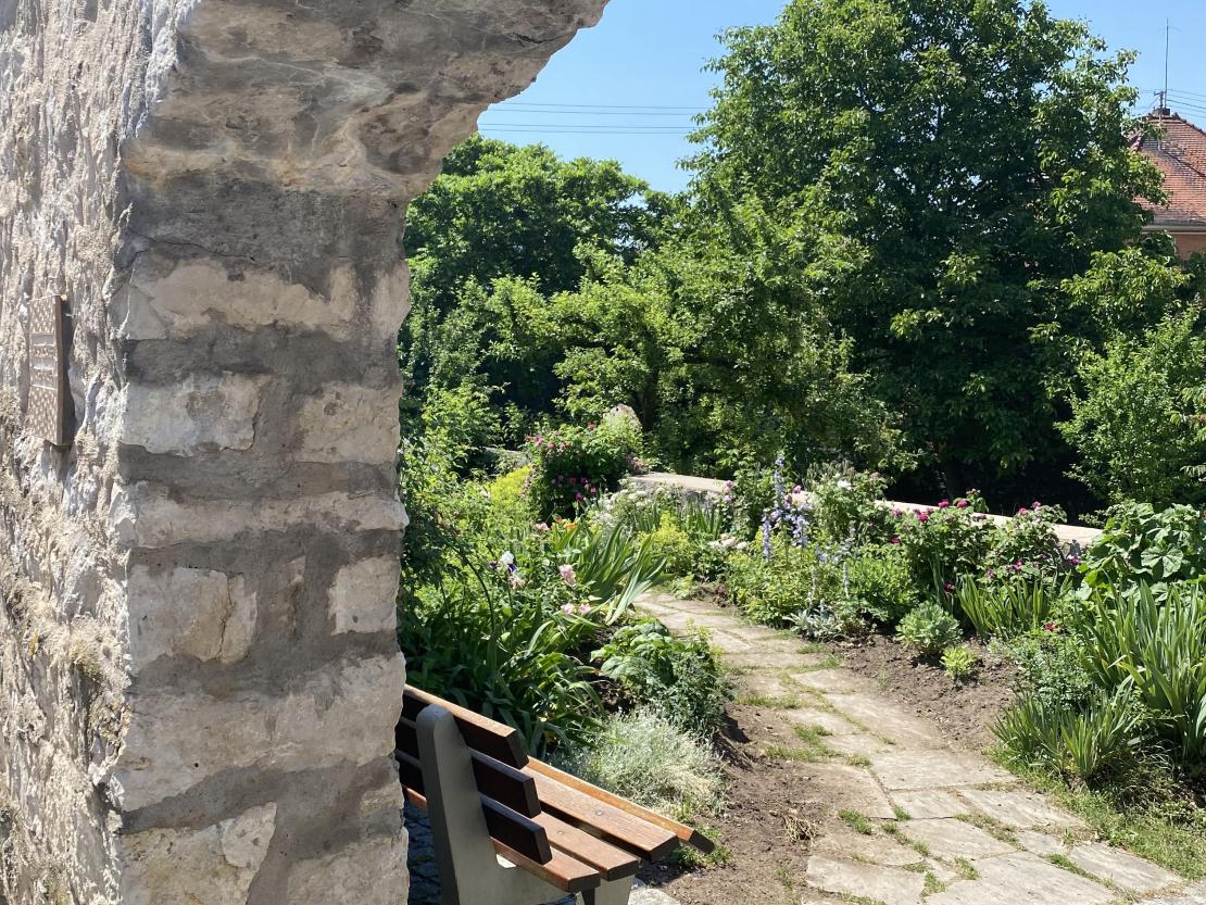 Wenn man geradeaus durch den Torbogen läuft, wird man von einem Meer von duftenden Blumen und Sträuchern begrüßt und förmlich dazu eingeladen, sich auf der Bank auszuruhen. 