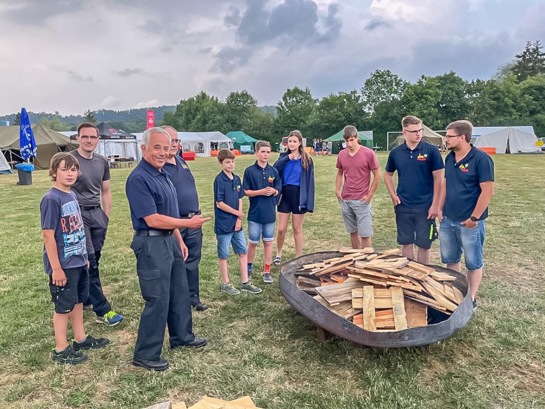 Kreisbrandrat Rudolf Mieling zusammen mit dem örtlich zuständigen Kreisbrandinspektor Heinz Mayr und einer Gruppe Jugendlicher beim Entzünden des Lagerfeuers. 