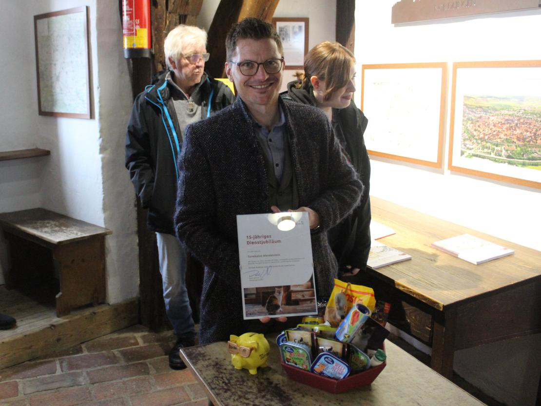 Hier sieht man Nördlingens Oberbürgermeister mit Urkunde und Präsentkorb für Turmkatze Wendelstein.