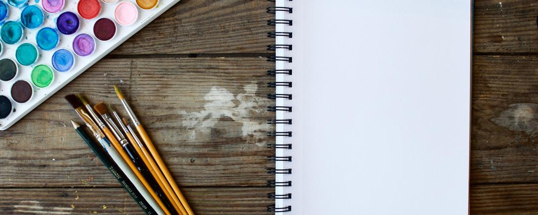 Auf dem Bild ist ein Zeichenblock, Aquarell und Pinsel zu sehen. 