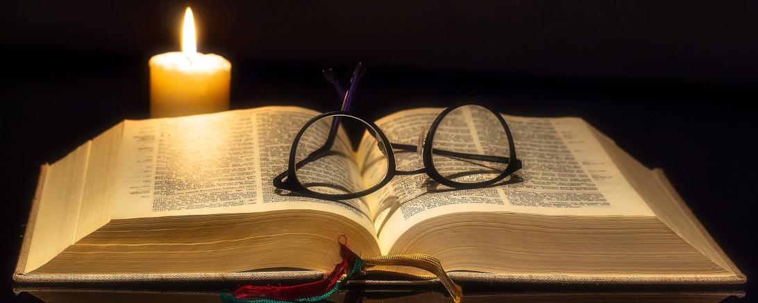 Das Bild zeigt eine Aufgeschlagene Bibel und eine Brille. 
