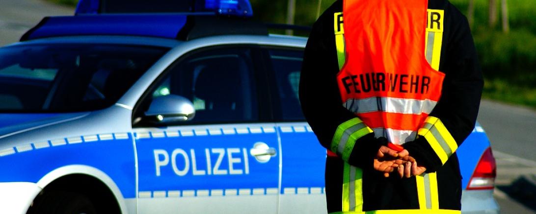 Das Bild zeigt ein Polizeiauto und einen Feuerwehrmann. 