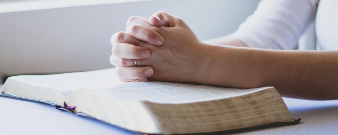 Frau hat ihre Hände gefaltet und betet auf einer Bibel